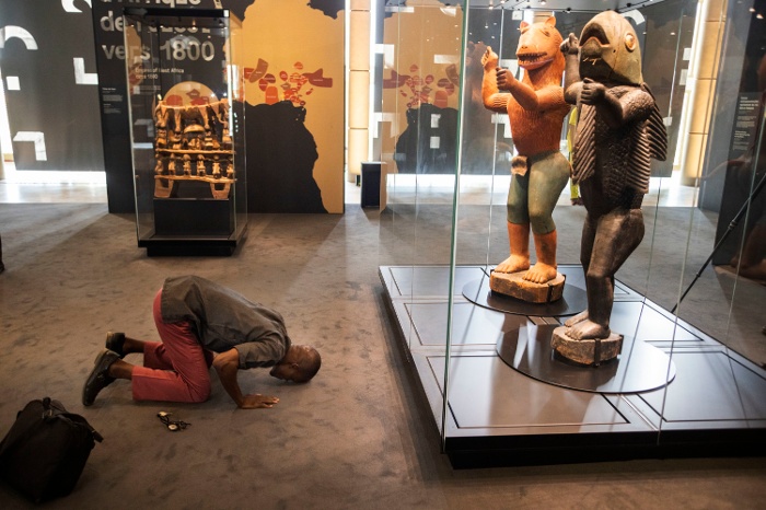 A man kneels in front of the statue of Behanzin at the exhibition opening, Cotonou, Benin, 2022. Courtesy of Patrick Zachmann/ Magnum Photos